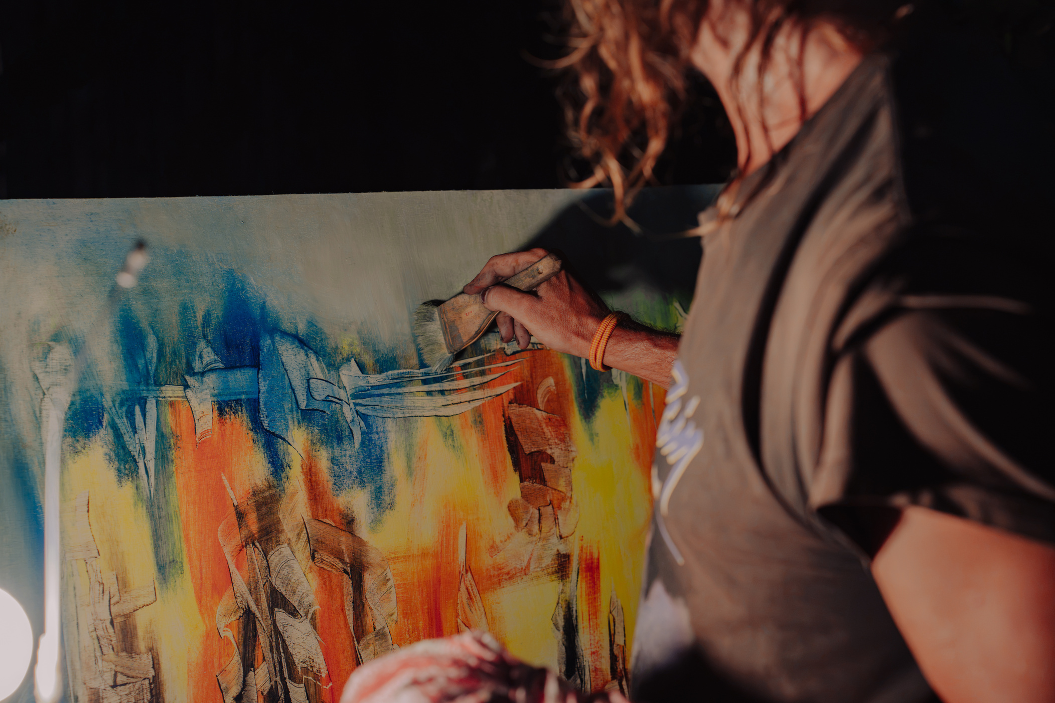 A painter working on a large canvas in blues and oranges