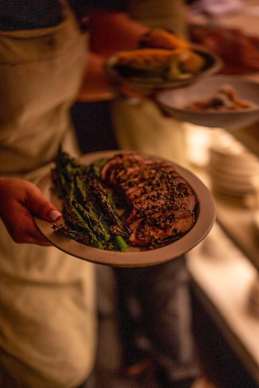 A plated dish of sliced meat and grilled greens carried to the table